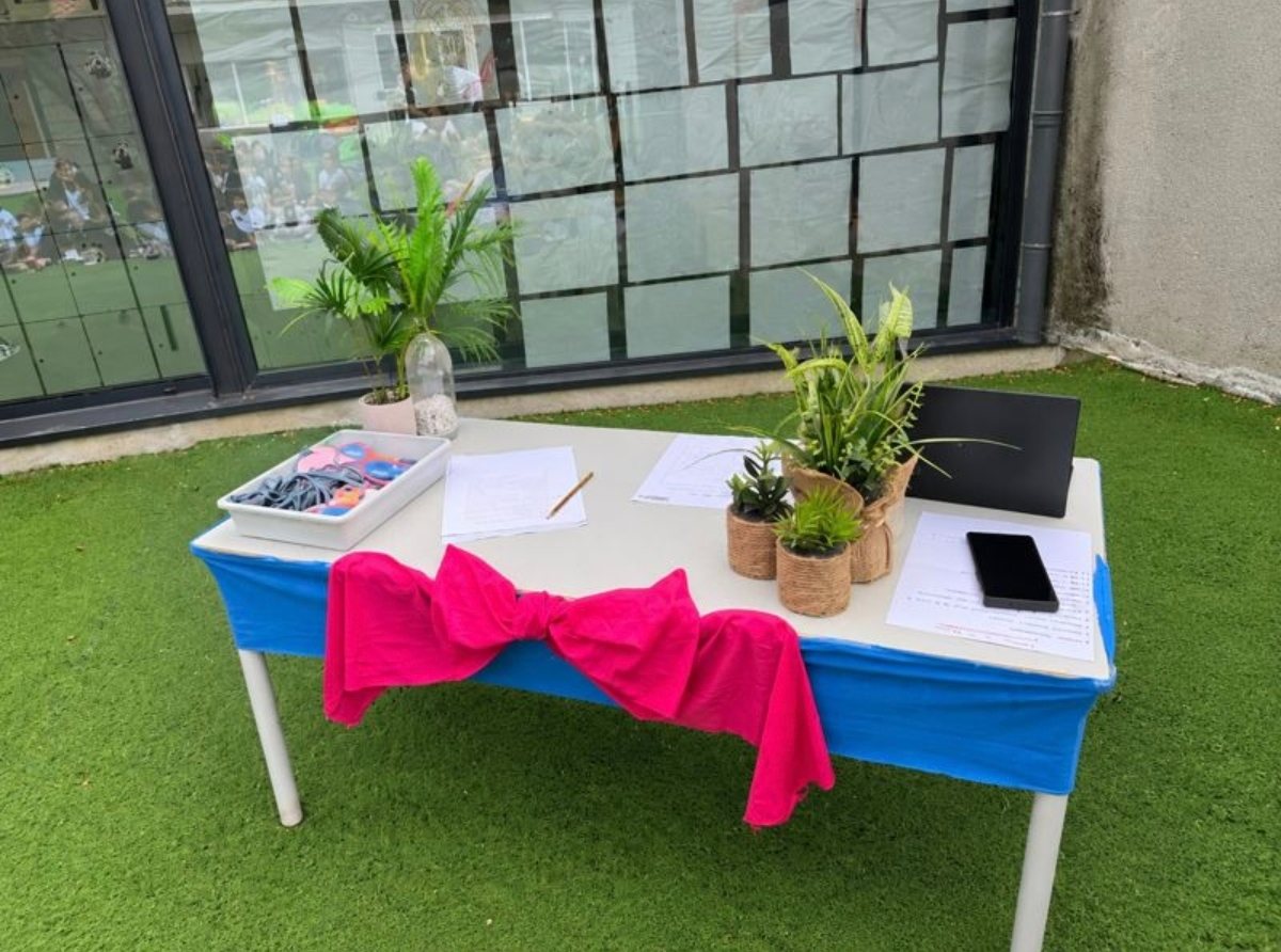 Mesa preparada no recreio para a School Assembly, com plantas, folhas de registo e as medalhas dos alunos